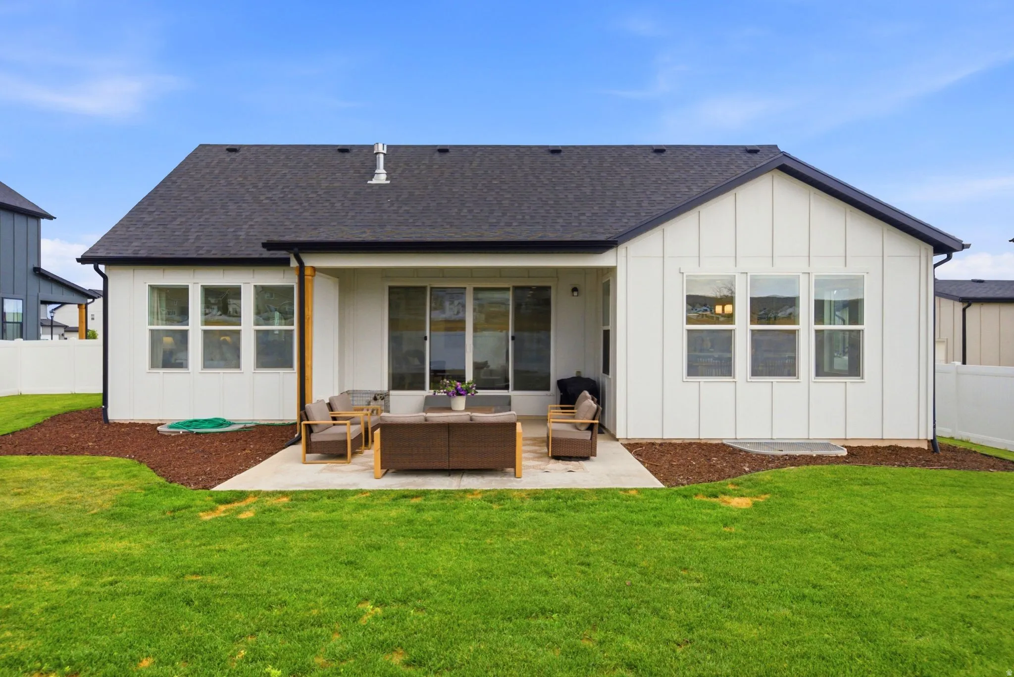 Rear exterior featuring a concrete patio, board and batten siding, multiple pane windows, a dark shingled roof, and a green lawn