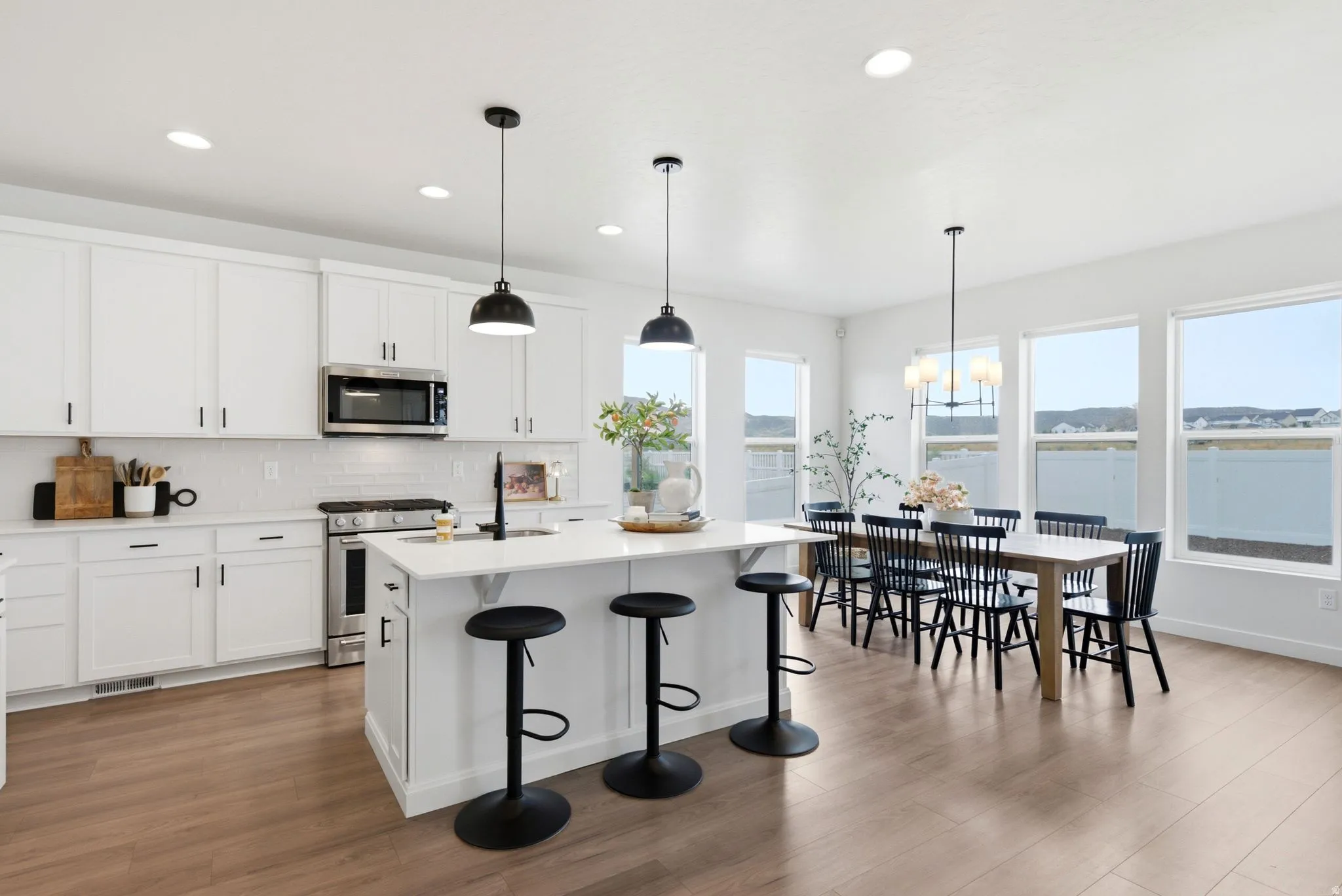 Open-concept kitchen and dining area featuring white shaker cabinetry, stainless steel appliances, a white subway tile backsplash, a center island with a white countertop, and wood-finish flooring