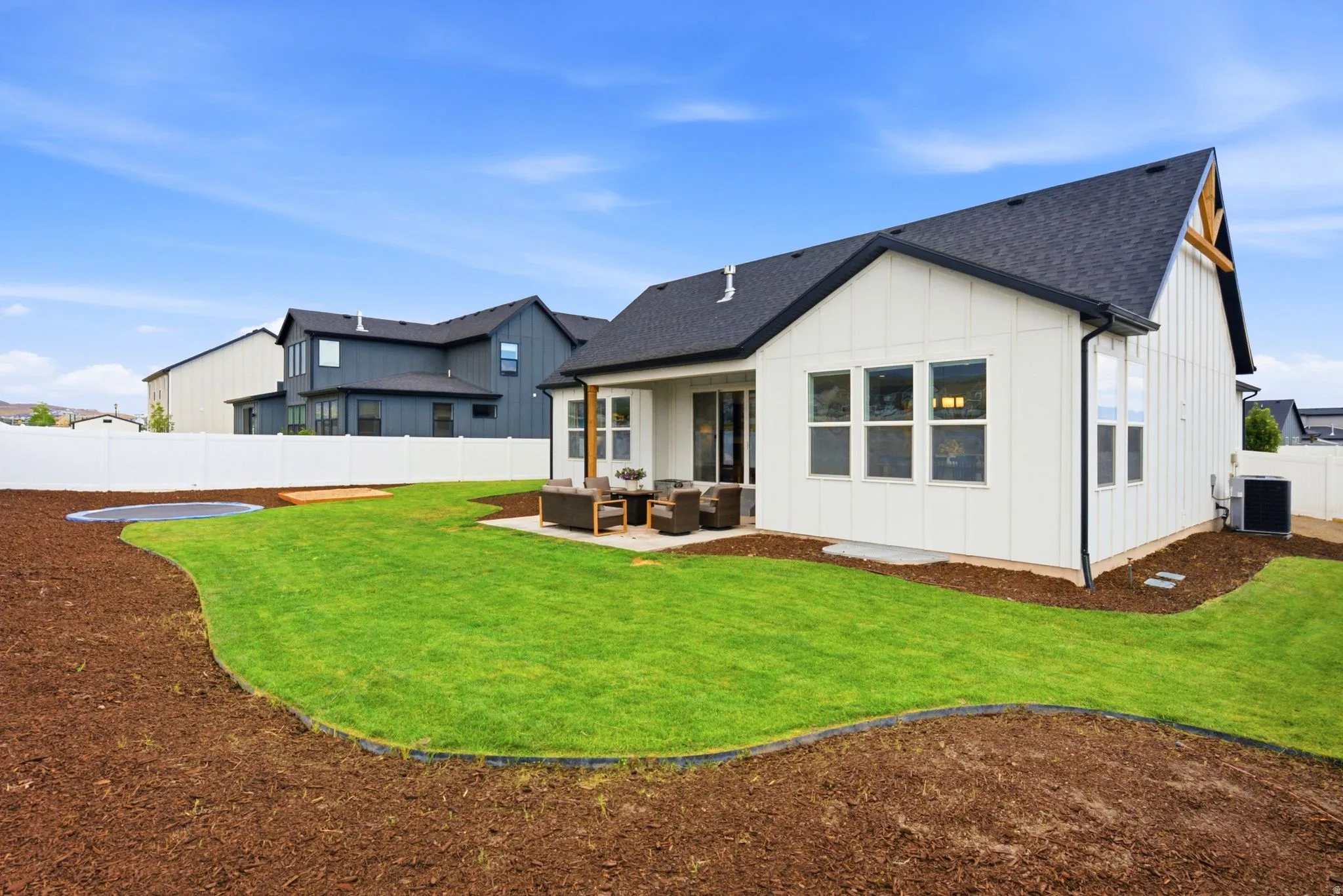Expansive backyard featuring a manicured lawn, fresh bark landscaping, and a white privacy fence
