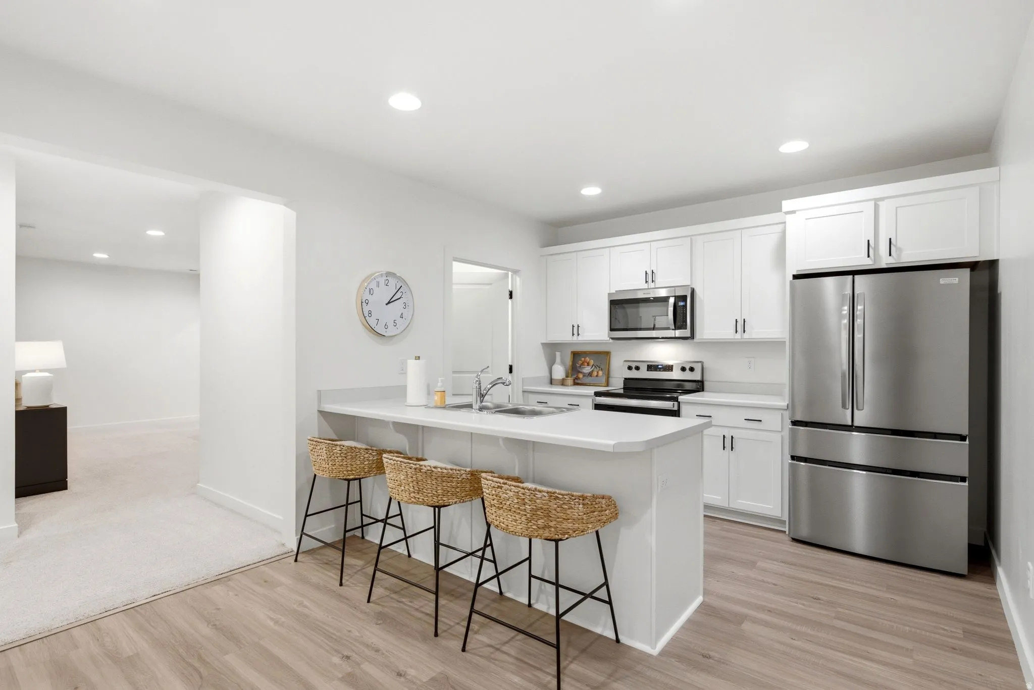 Kitchen featuring a peninsula with countertop seating, white shaker-style cabinetry, stainless steel appliances, wood-finish flooring, and recessed lighting