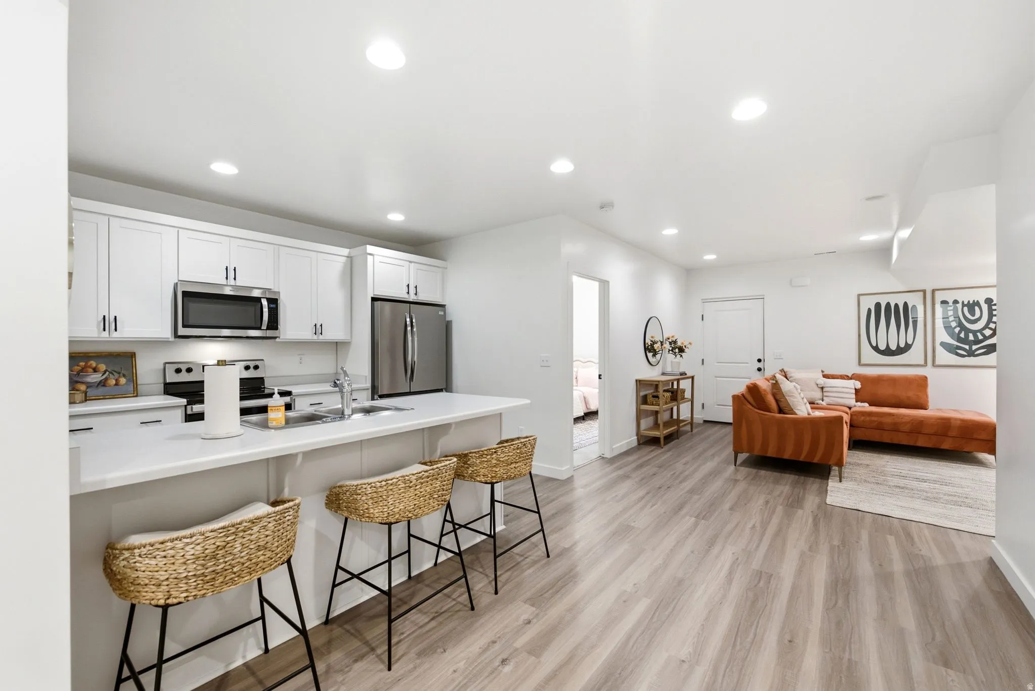 Open-concept living area featuring wood-finish flooring, recessed lighting, and a white kitchen island with an integrated sink