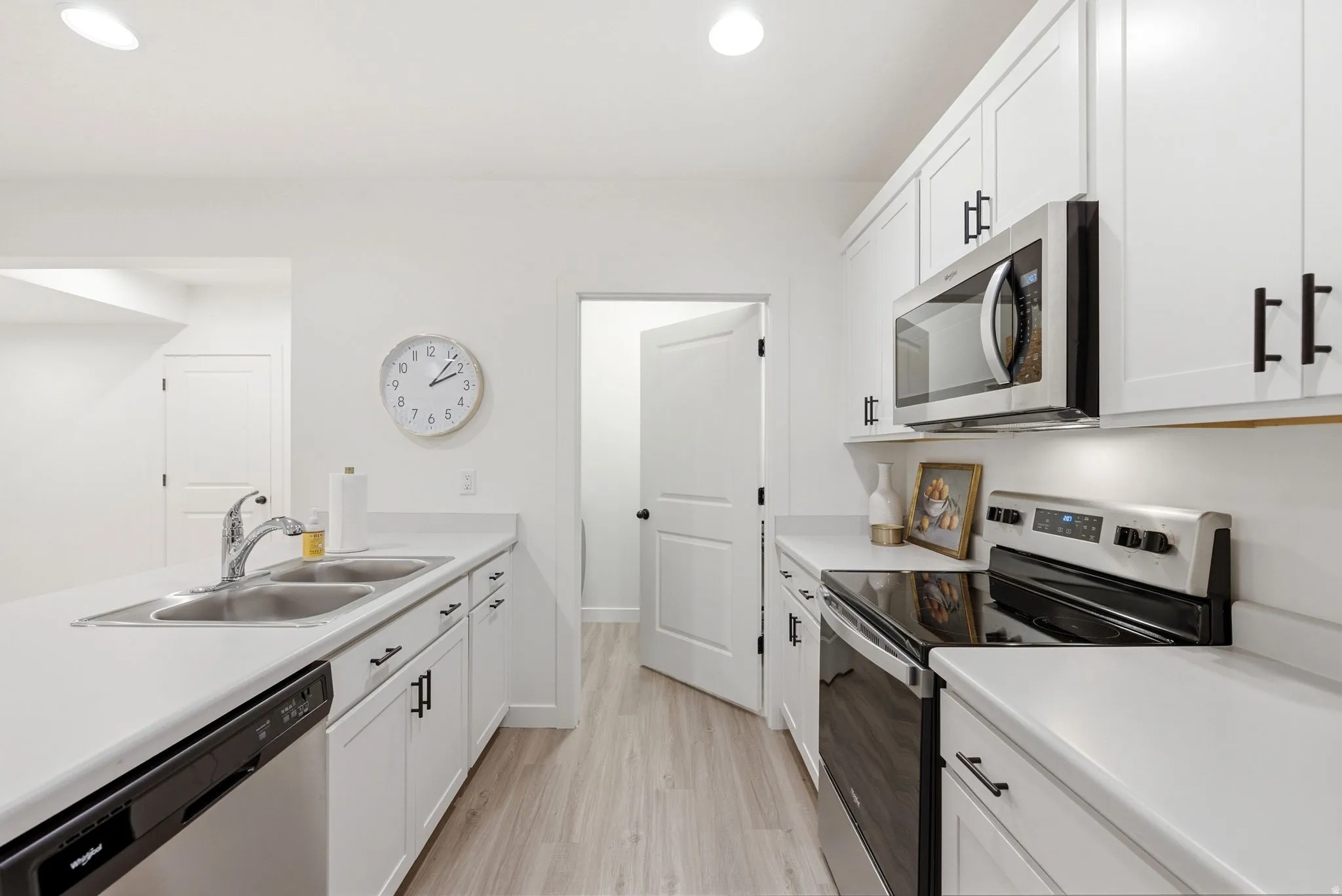 Modern kitchen featuring white cabinetry with black hardware, light-toned countertops, and stainless steel appliances including a built-in microwave and electric range
