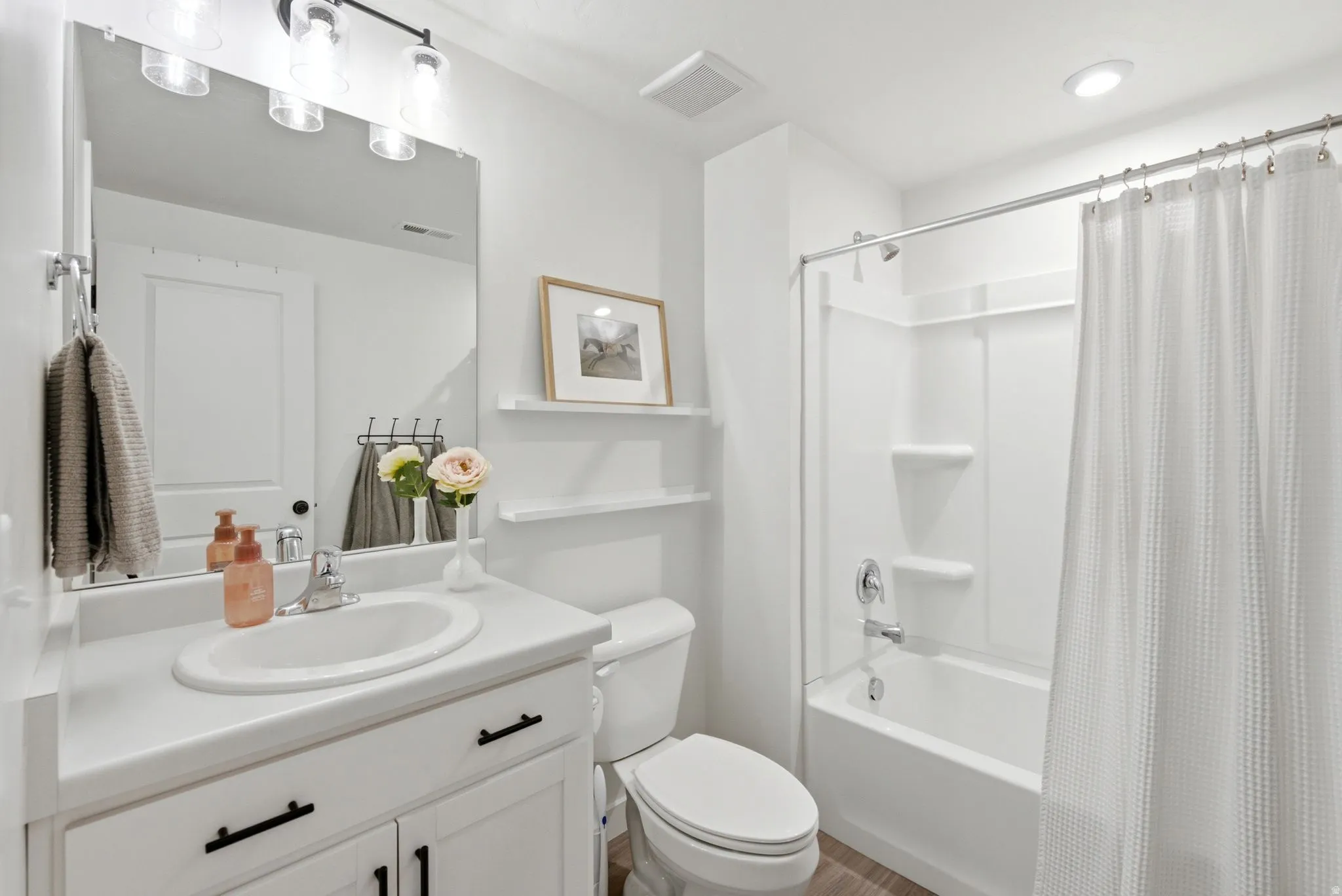 Bathroom featuring a white vanity with an integrated sink, black hardware, a rectangular mirror, and a three-light fixture