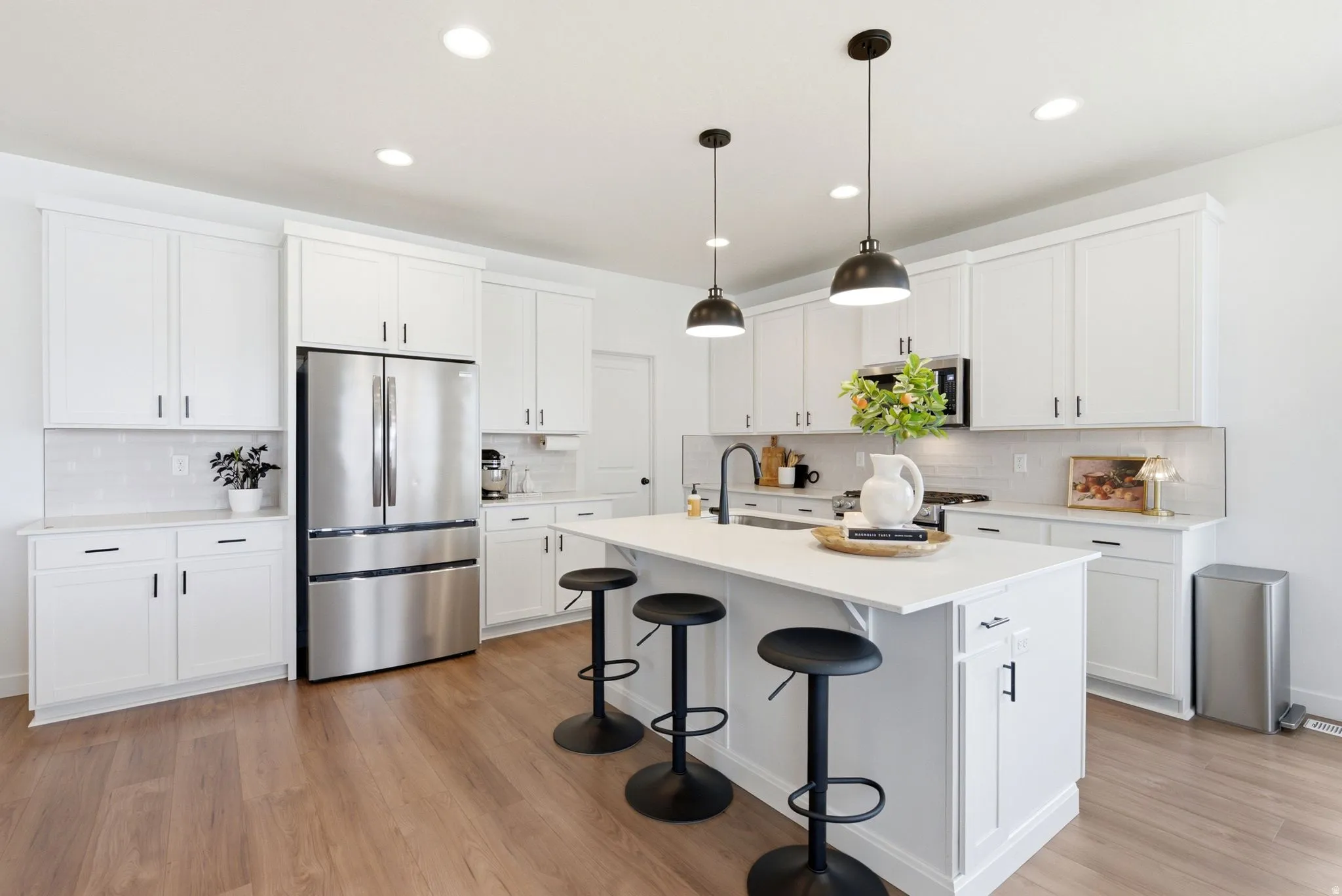 Modern kitchen featuring an expansive center island with seating, white shaker-style cabinetry, stainless steel appliances, wood-finish flooring, and pendant lighting