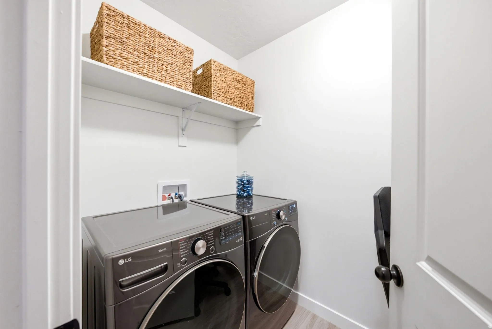 Dedicated laundry area featuring a white wall shelf, contemporary wood-finish flooring, and a door with black hardware