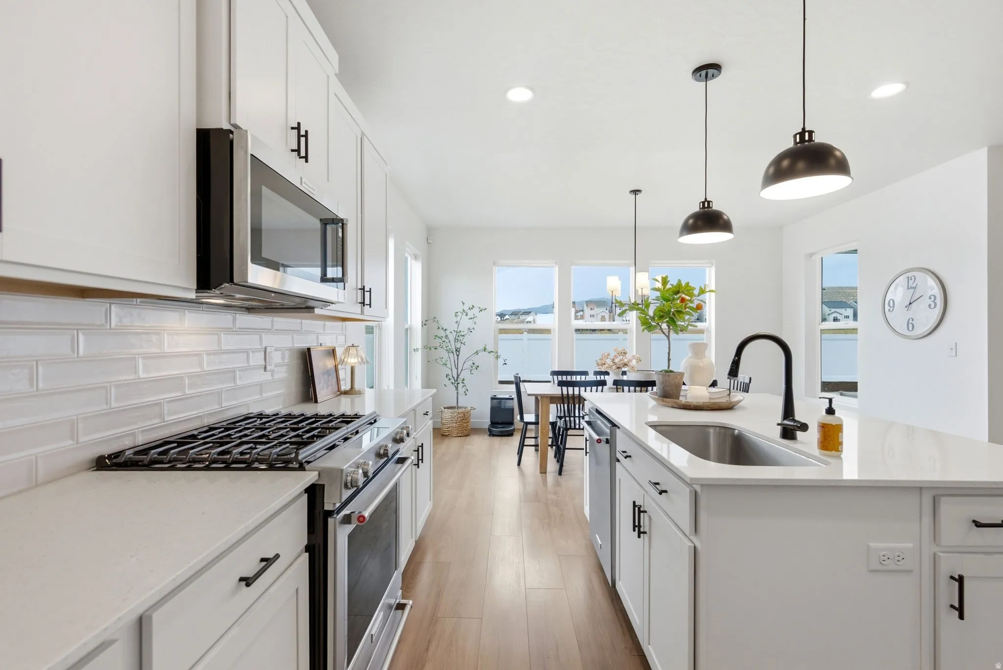 Modern kitchen featuring white cabinetry with black hardware, stainless steel appliances, light countertops, and a subway tile backsplash
