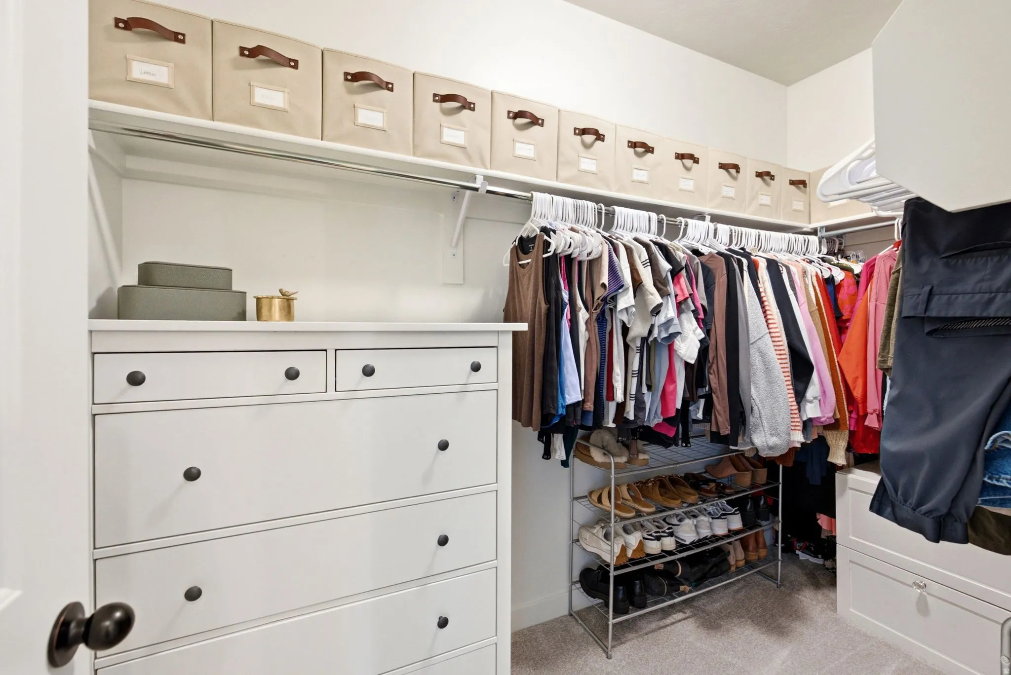 Walk-in closet featuring built-in white dresser cabinetry, upper shelving, and extensive hanging rods