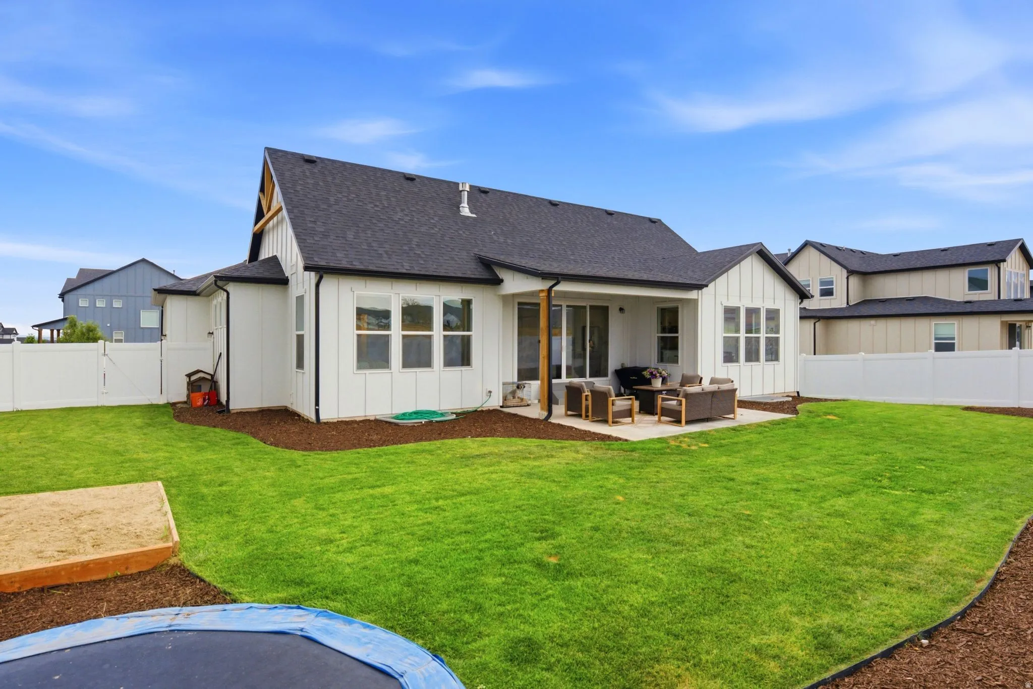 Expansive backyard featuring a lush lawn, white vinyl fencing, and a concrete patio