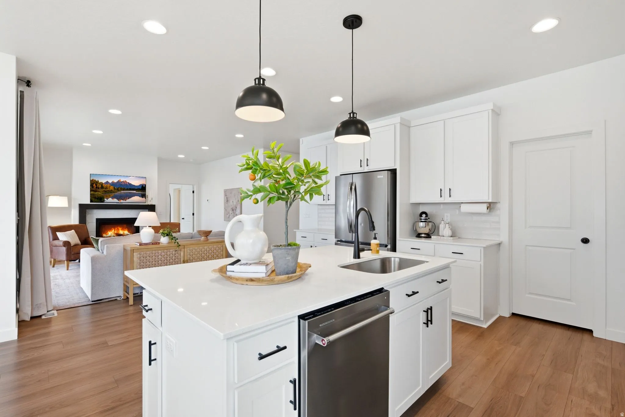 Open-concept kitchen featuring an oversized island with an undermount sink, pendant lighting, white cabinetry with black hardware, and wood-finish flooring