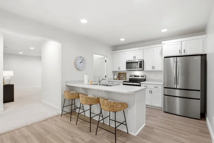 Kitchen featuring a peninsula with countertop seating, white shaker-style cabinetry, stainless steel appliances, wood-finish flooring, and recessed lighting