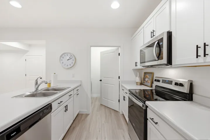 Modern kitchen featuring white cabinetry with black hardware, light-toned countertops, and stainless steel appliances including a built-in microwave and electric range