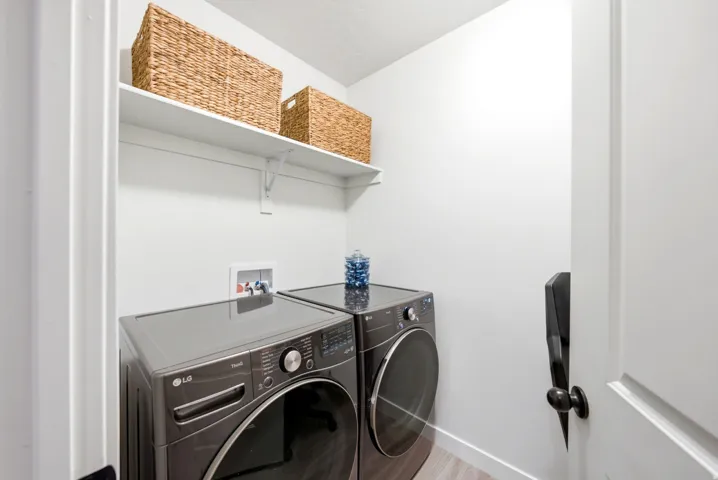 Dedicated laundry area featuring a white wall shelf, contemporary wood-finish flooring, and a door with black hardware