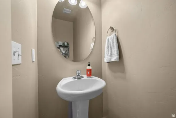Pedestal sink with chrome faucet, complemented by an oval wall mirror and built-in vanity lighting