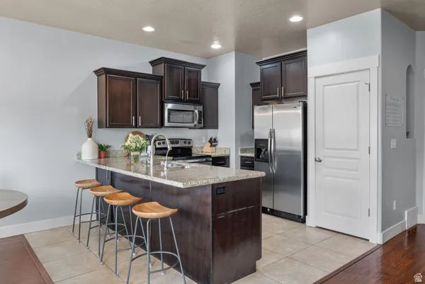 Kitchen featuring a large island with stone countertop, dark wood cabinetry, stainless steel appliances, and recessed lighting