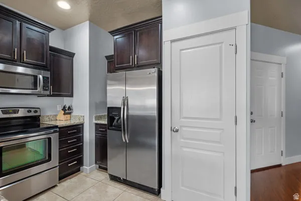 Kitchen featuring stainless steel appliances, dark wood-finish cabinetry, light-toned granite countertops, and tile flooring