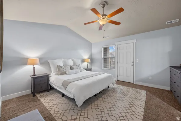 Vaulted ceiling bedroom featuring a ceiling fan with integrated lighting, window with blinds, paneled door, and carpet flooring