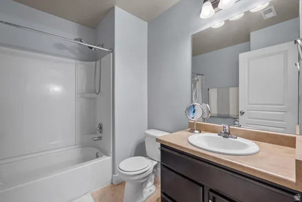 Full bathroom featuring a white tub/shower combination, dark wood-finish vanity with a light-toned countertop, integrated sink, and an overhead vanity light fixture