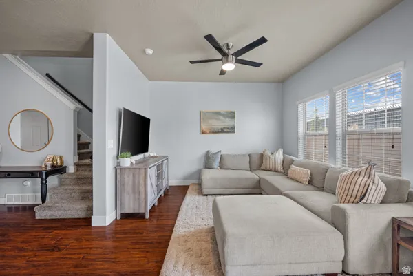 Open-concept living area featuring wood-finish flooring, a vaulted ceiling with a contemporary ceiling fan, and multiple windows with blinds