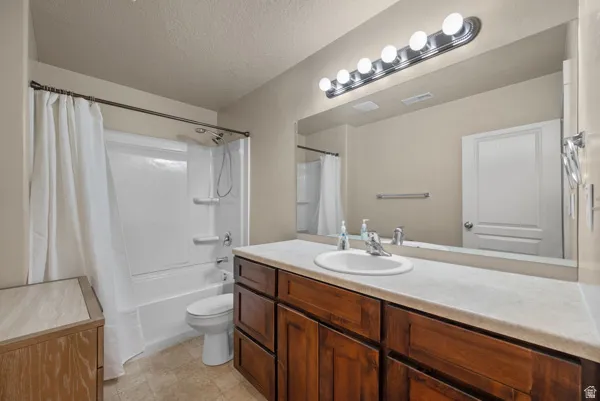 Spacious bathroom featuring a single vanity with a solid surface countertop and wood cabinetry, a large mirror with overhead vanity lighting, and a white tub/shower combination