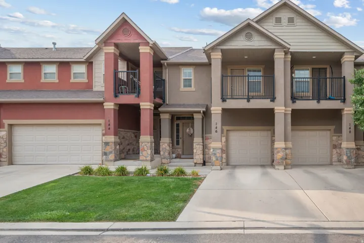 Multi-level townhome exterior featuring an attached garage, stone accents, and a second-story balcony with metal railing