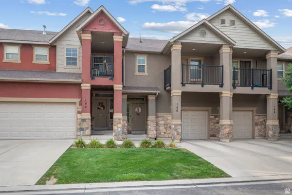 Townhome exterior featuring varied siding materials, stone accents, multiple balconies with black railings, and attached garages