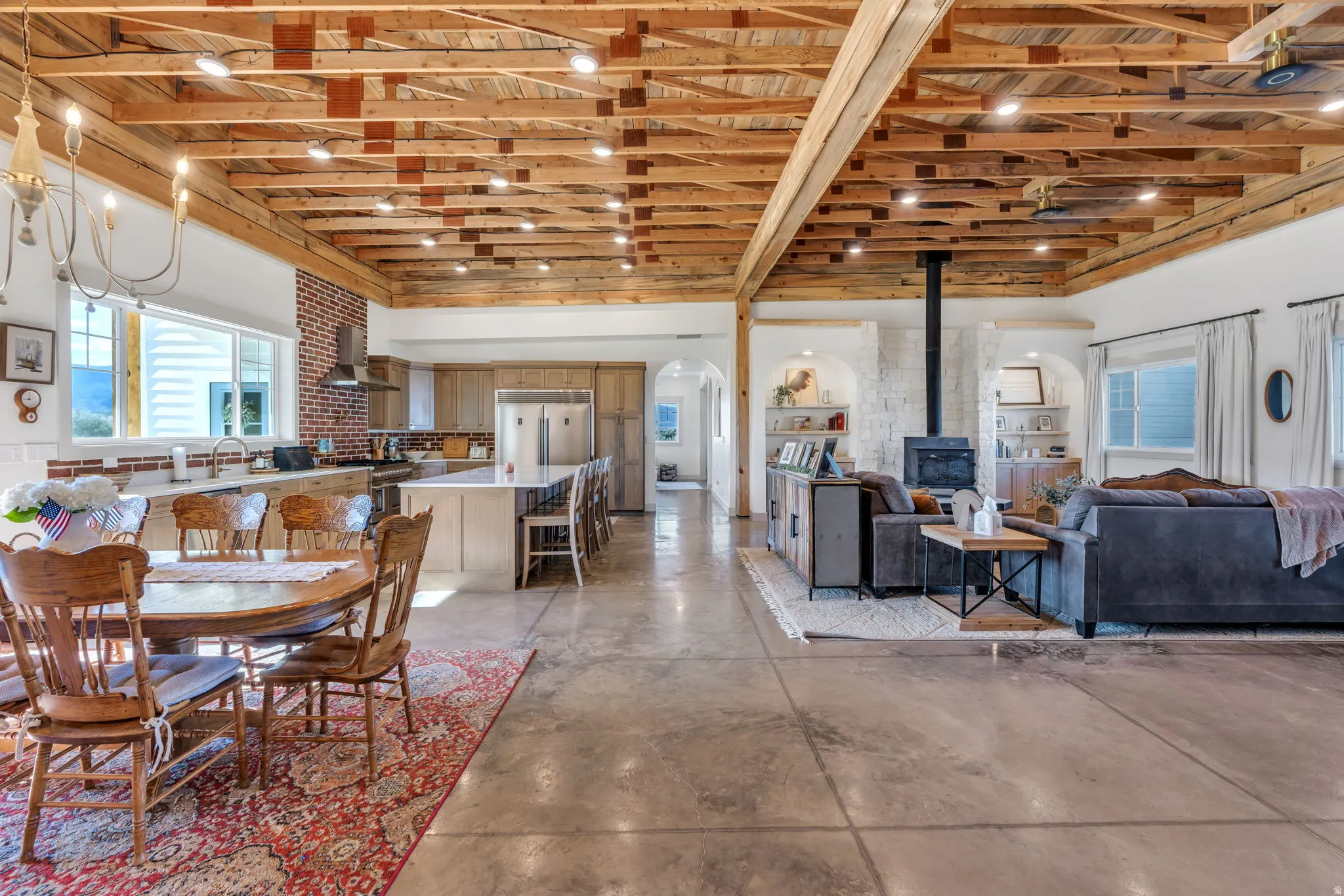 Open-concept living space featuring a beamed wood ceiling with recessed lighting, exposed brick accents, and light-tone flooring