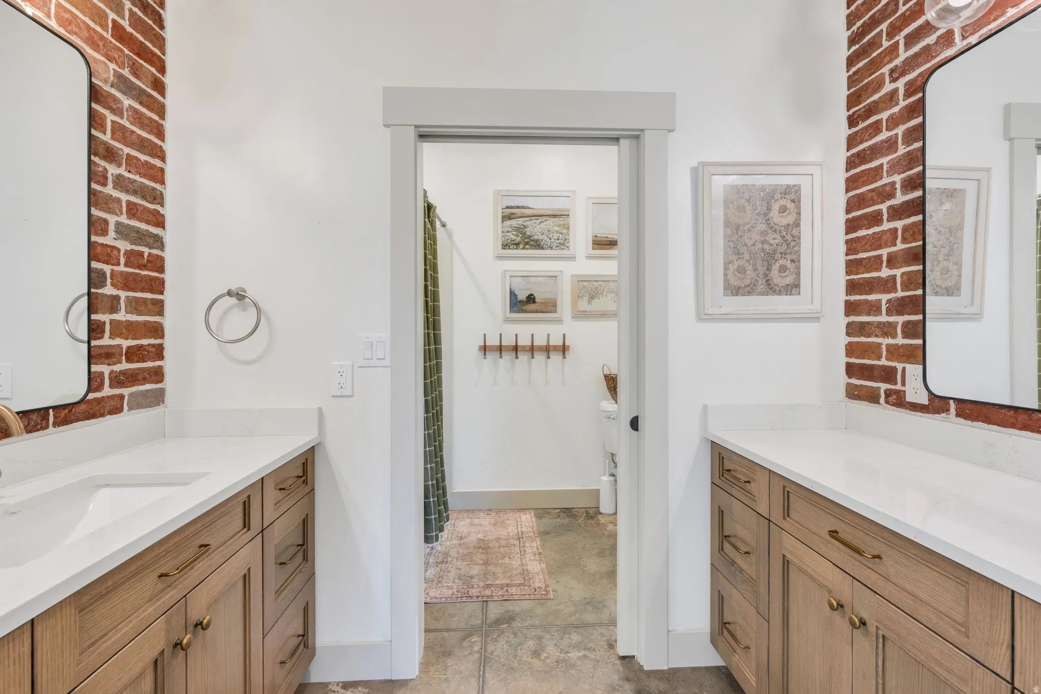 Dual vanity bathroom featuring exposed brick accents and white countertops
