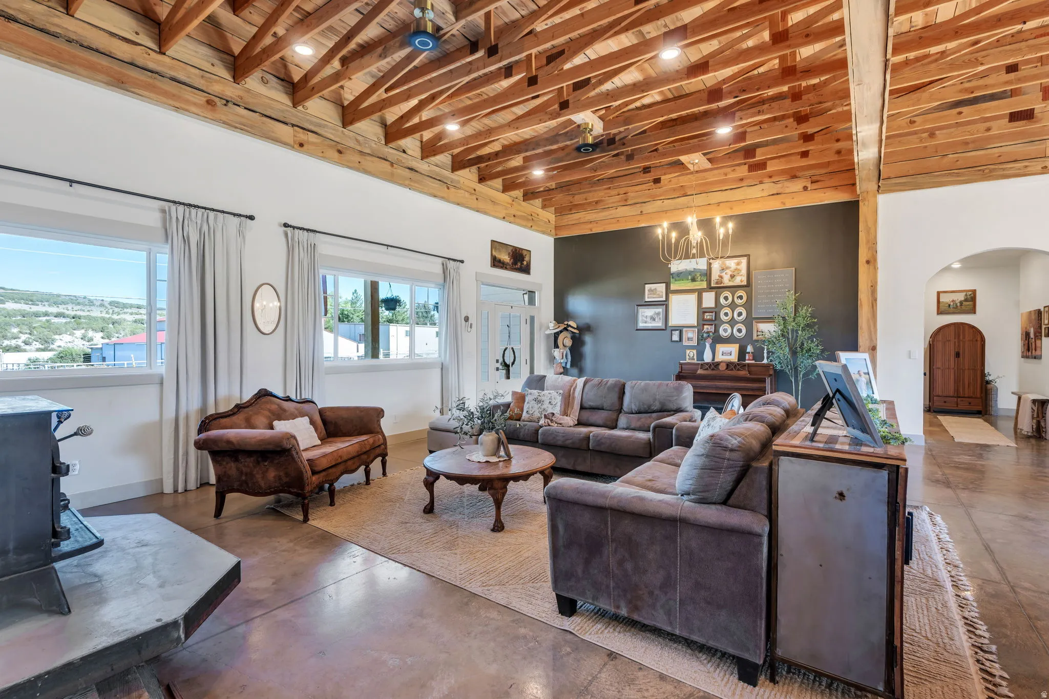 Spacious living area featuring an exposed beam and plank ceiling, polished concrete flooring, multiple windows providing natural light, a dark accent wall, and an arched entry