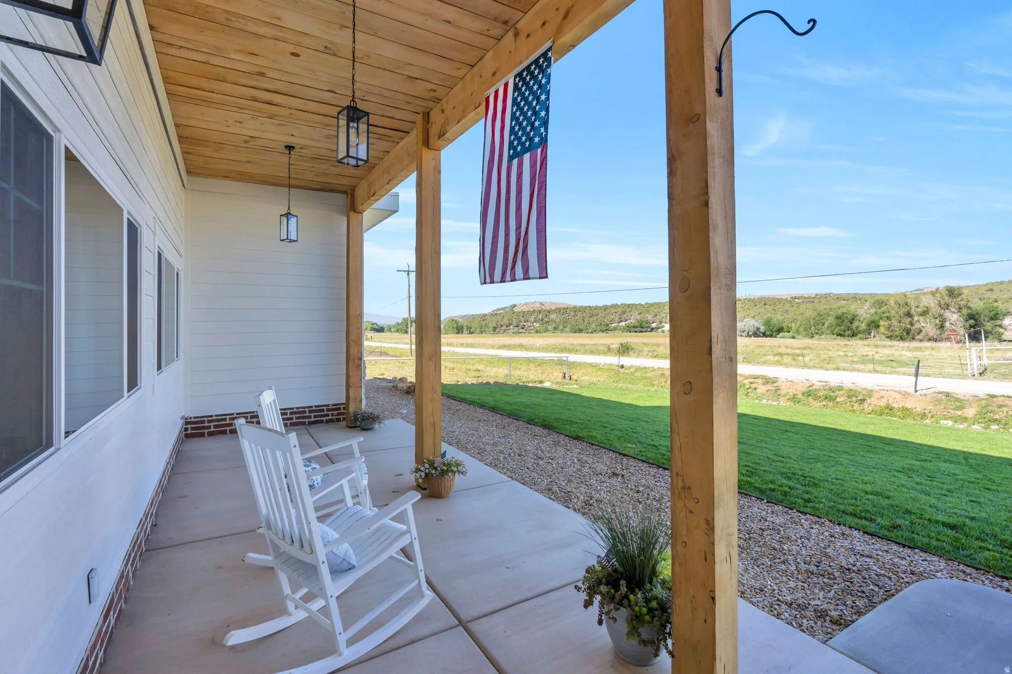 Expansive covered porch featuring a natural wood-finish ceiling, exposed wooden support beams, concrete flooring, and multiple windows