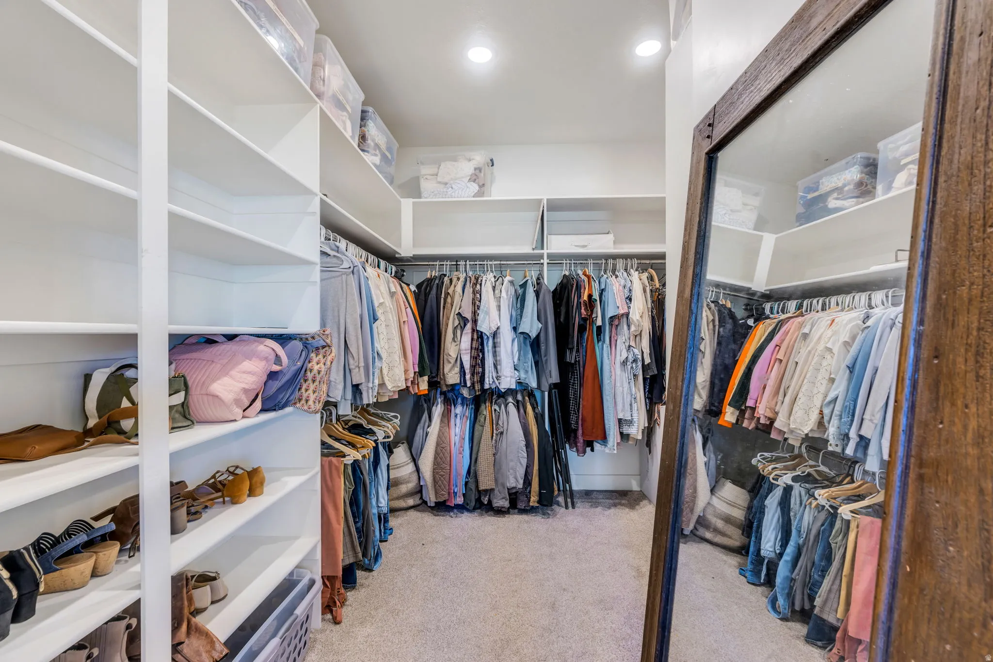 Expansive walk-in closet featuring extensive built-in shelving, multiple hanging rods, recessed lighting, and carpet flooring