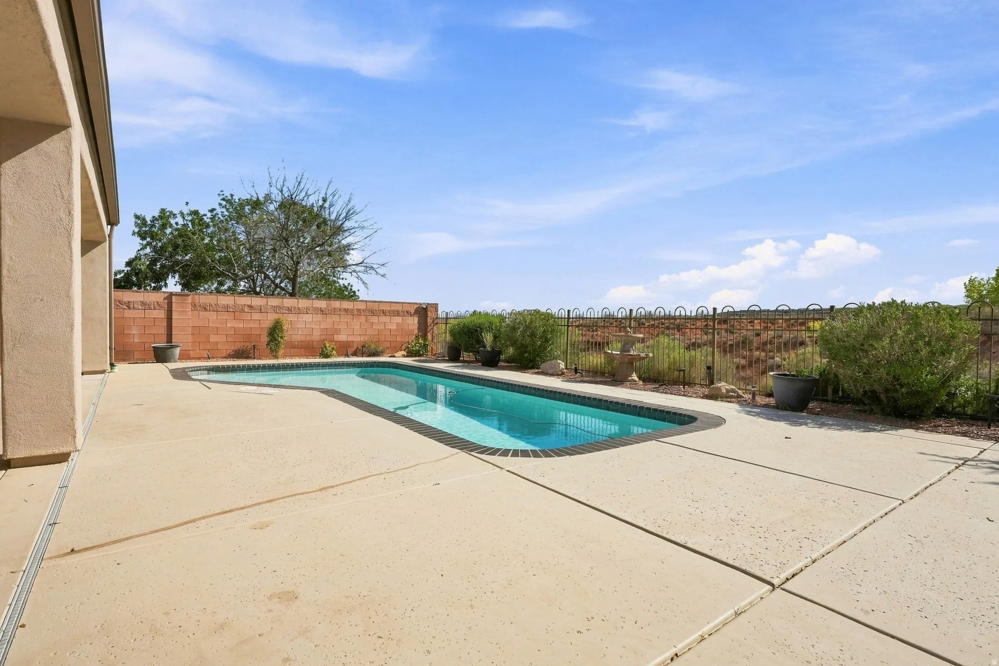Backyard featuring a rectangular swimming pool with brick coping, expansive concrete patio, and a brick privacy wall