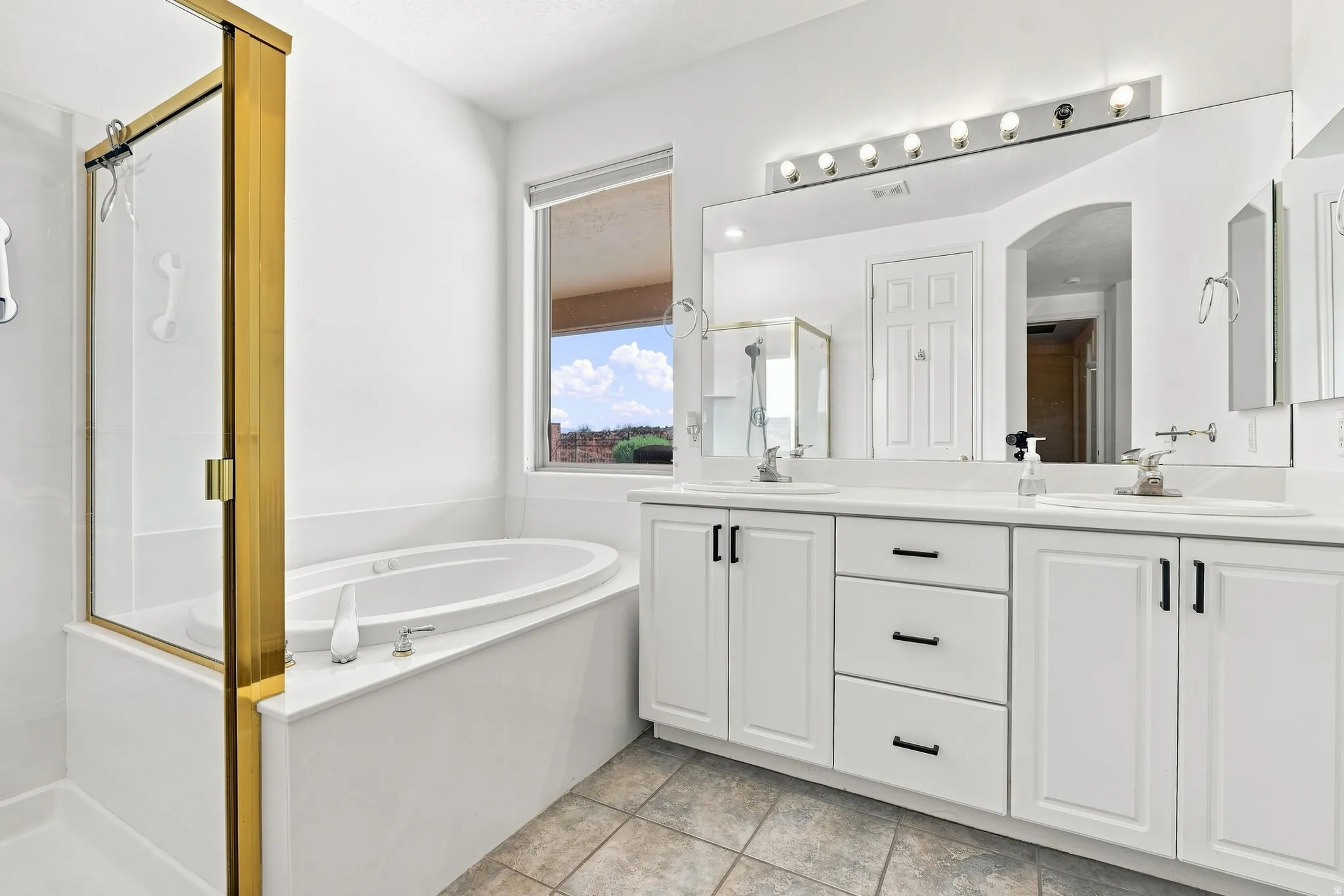 Spacious bathroom featuring a dual vanity with white cabinetry and dark hardware