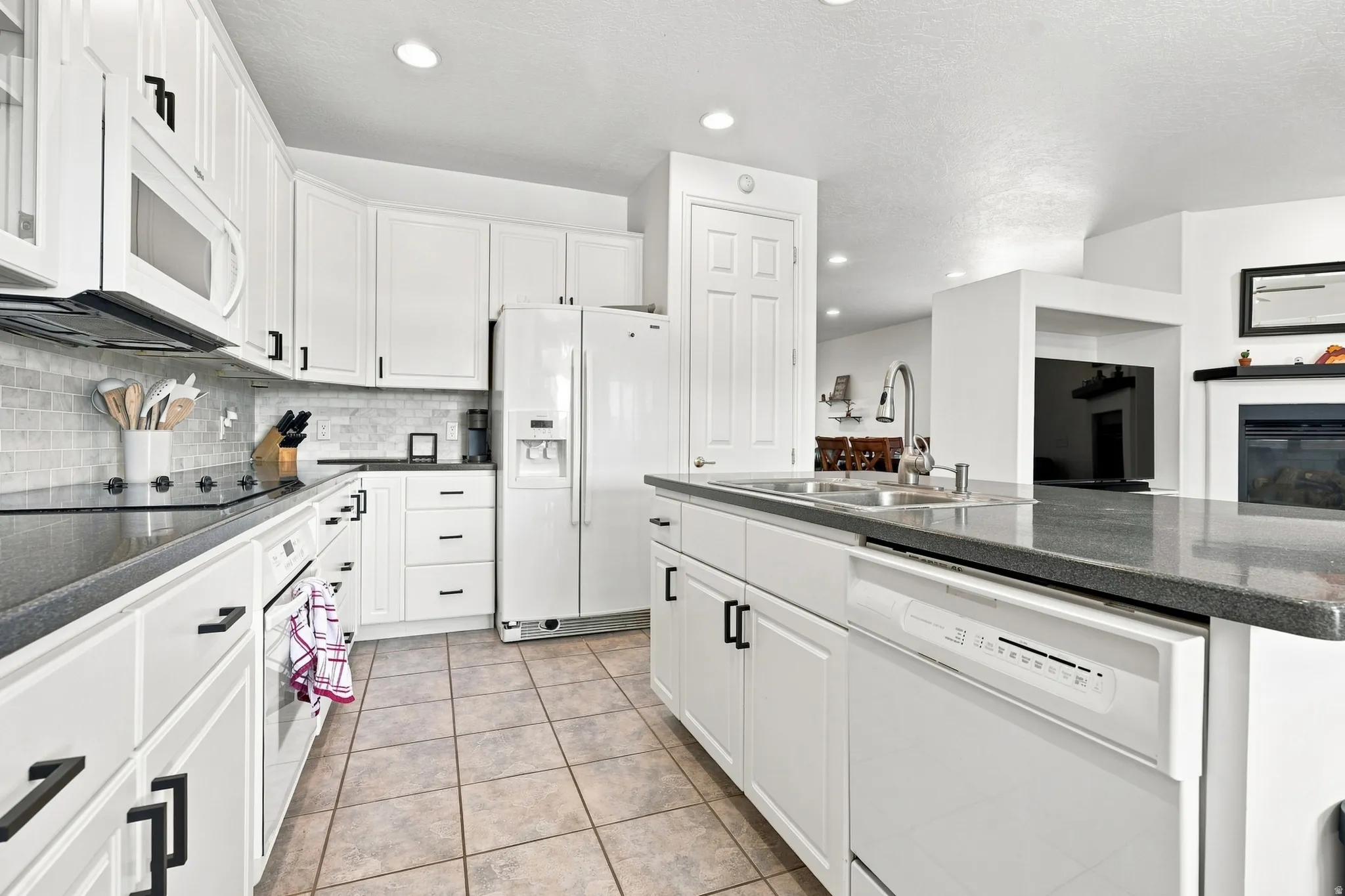 Modern kitchen featuring white cabinetry, dark countertops, a tile backsplash, and stainless steel appliances, including a built-in microwave and dishwasher