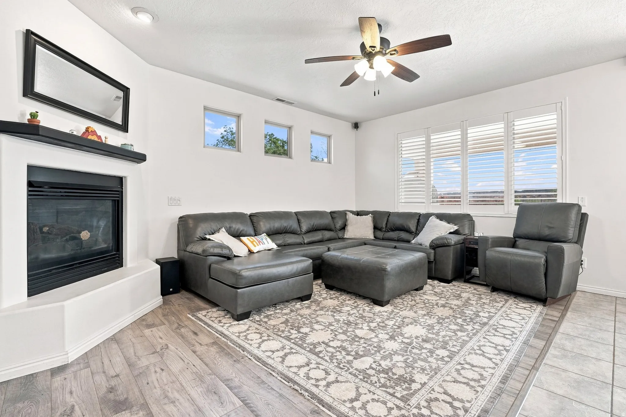 Living area featuring a corner fireplace with a black mantel, wood-finish flooring, and multiple windows with plantation shutters