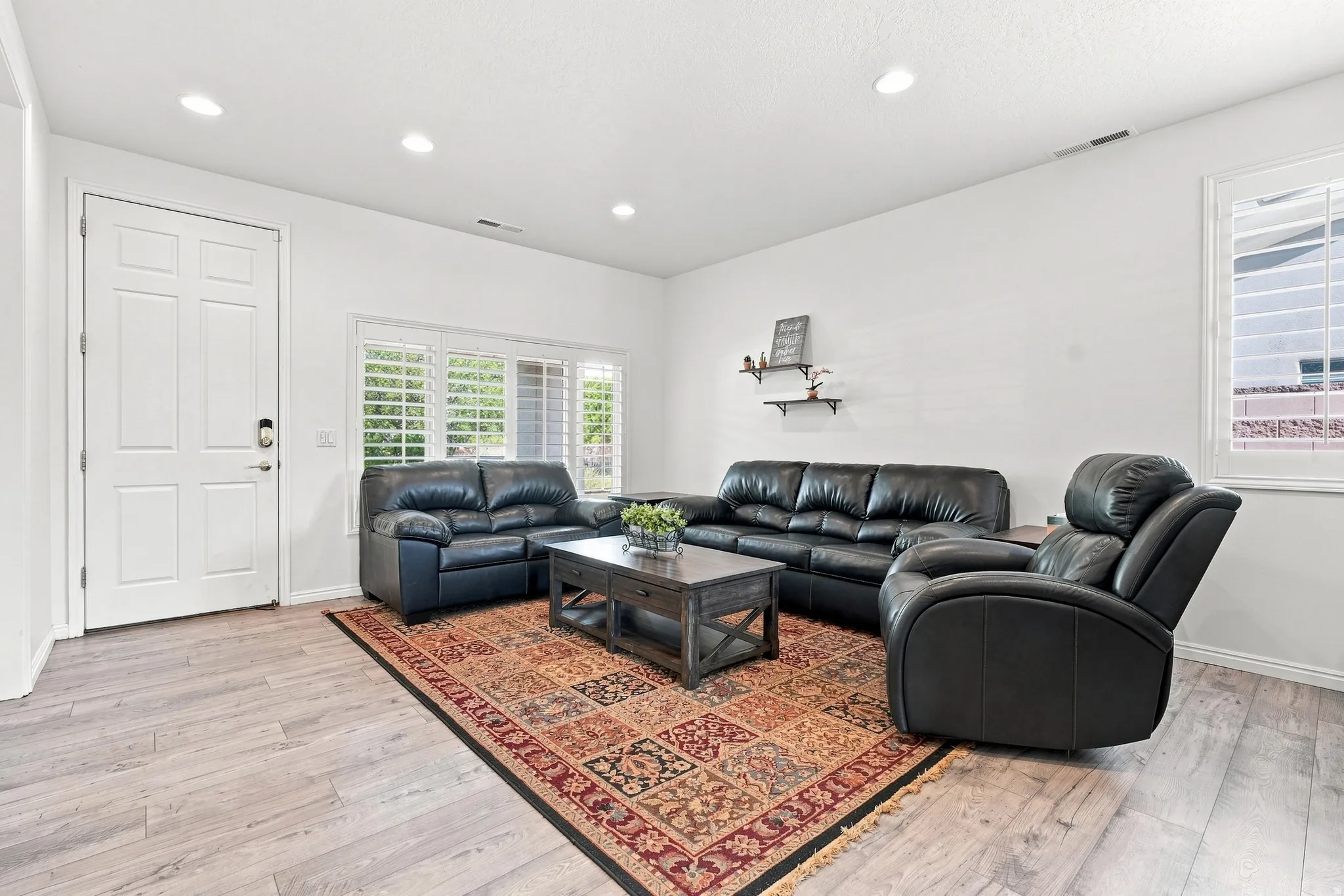 Bright living area featuring wood-finish flooring, white walls, recessed lighting, and windows with white plantation shutters