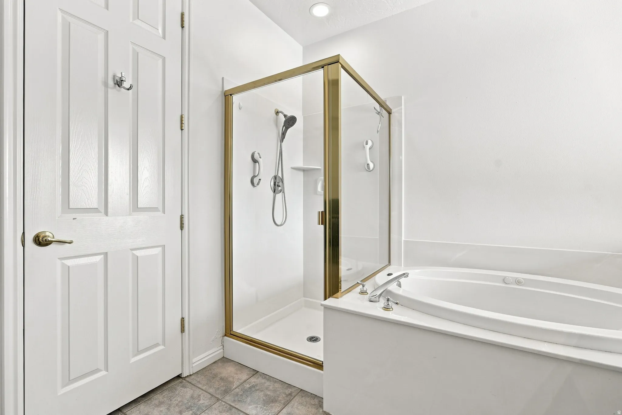 Bathroom featuring a built-in soaking tub with deck-mounted fixtures, enclosed shower with gold-tone frame, and panel-style door
