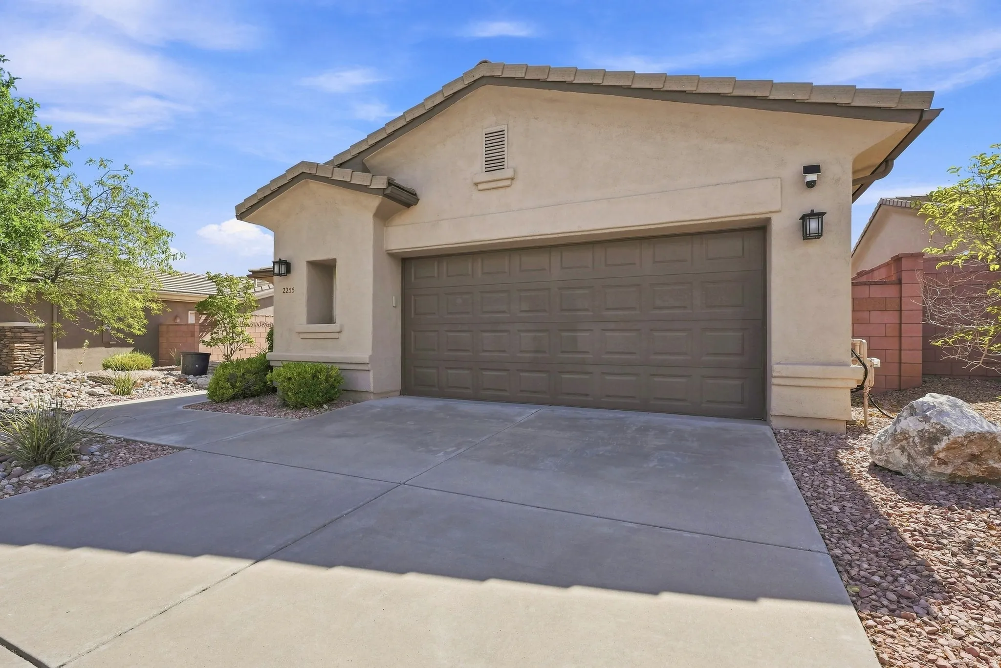 Stucco exterior with an attached garage featuring a panel door, concrete driveway, and desert-style landscaping