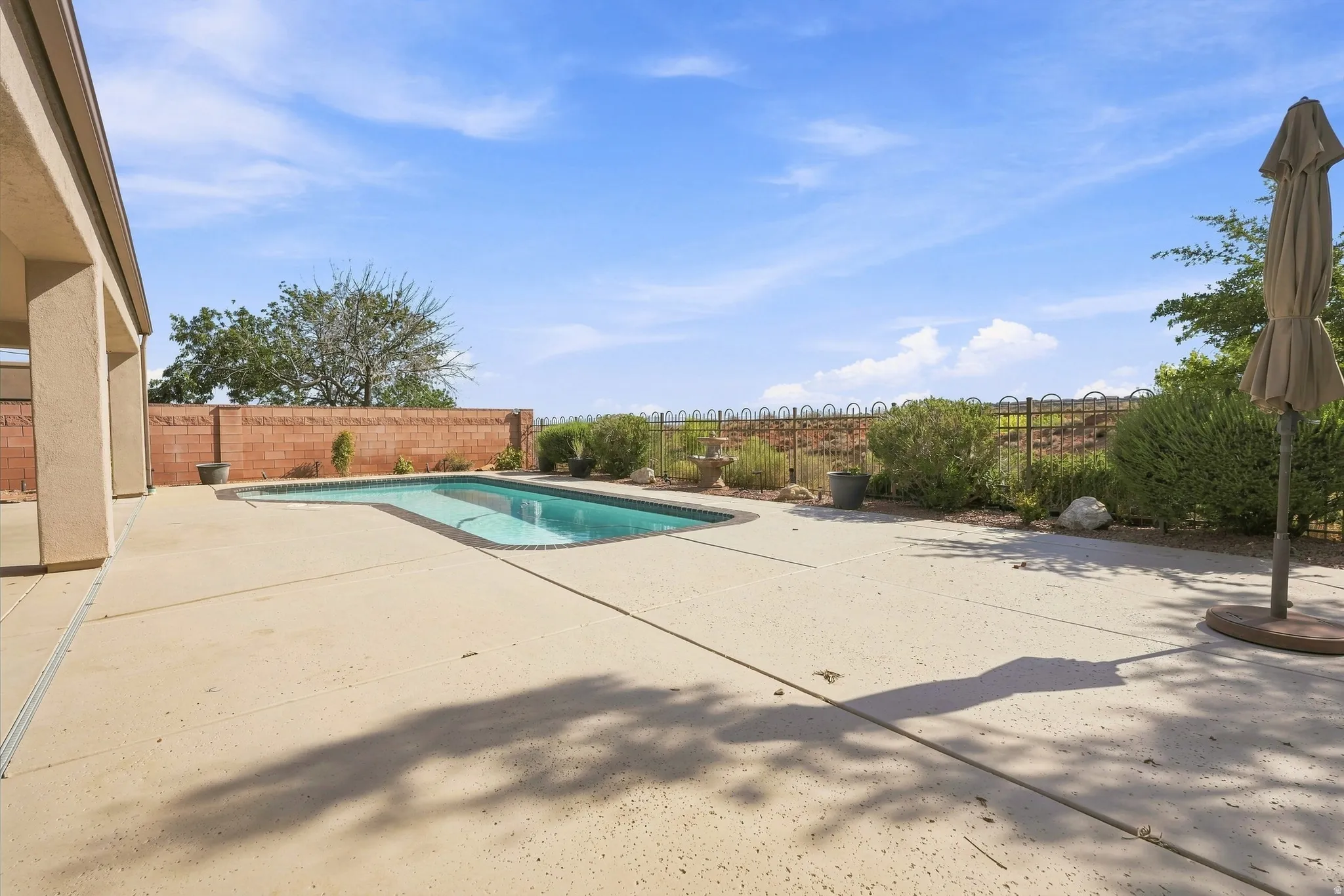 Outdoor swimming pool surrounded by a spacious concrete patio, a low brick privacy wall, and mature landscaping