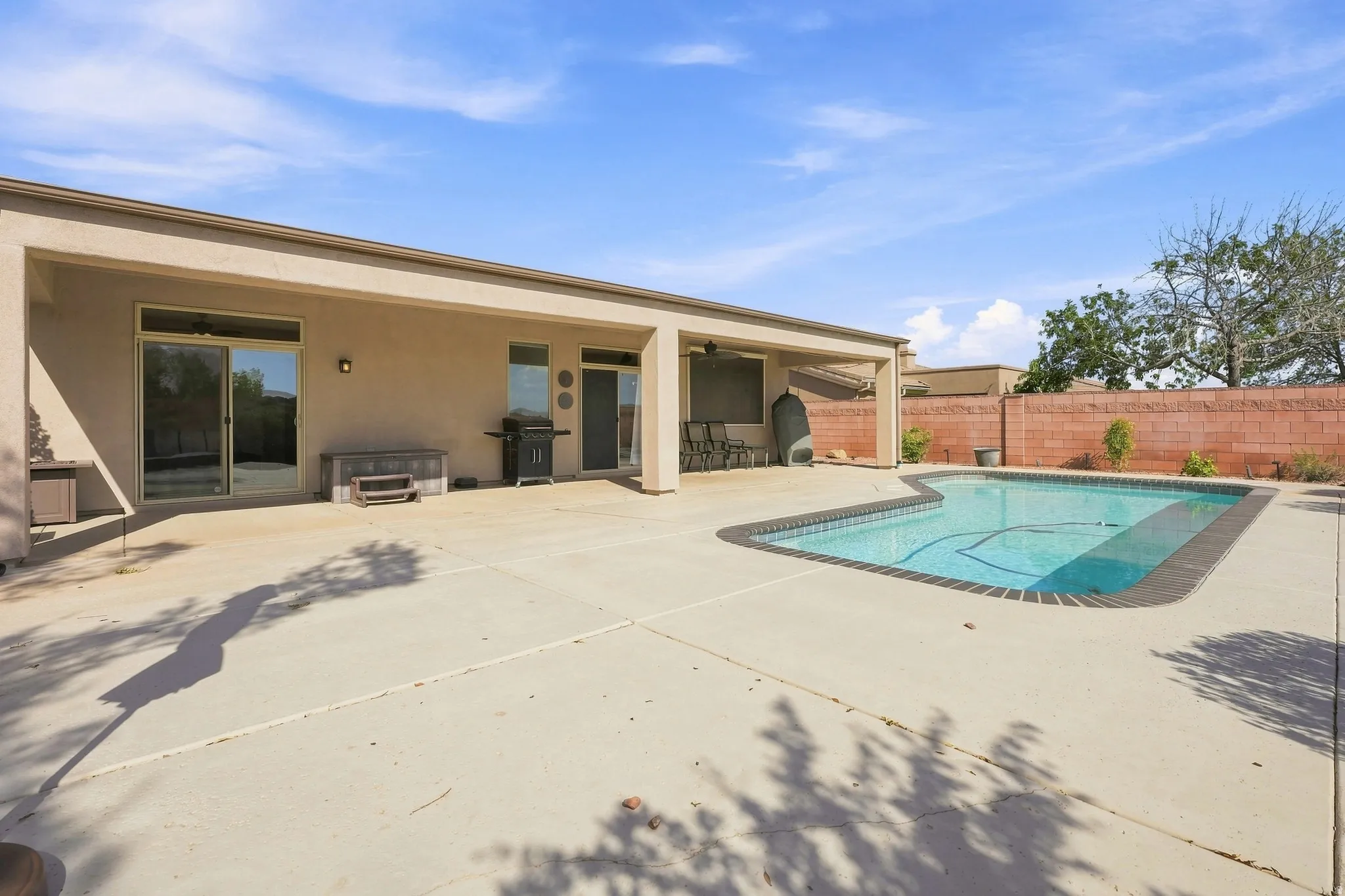 Expansive concrete patio area featuring a rectangular pool with blue tiling, a covered patio, and multiple sliding glass doors