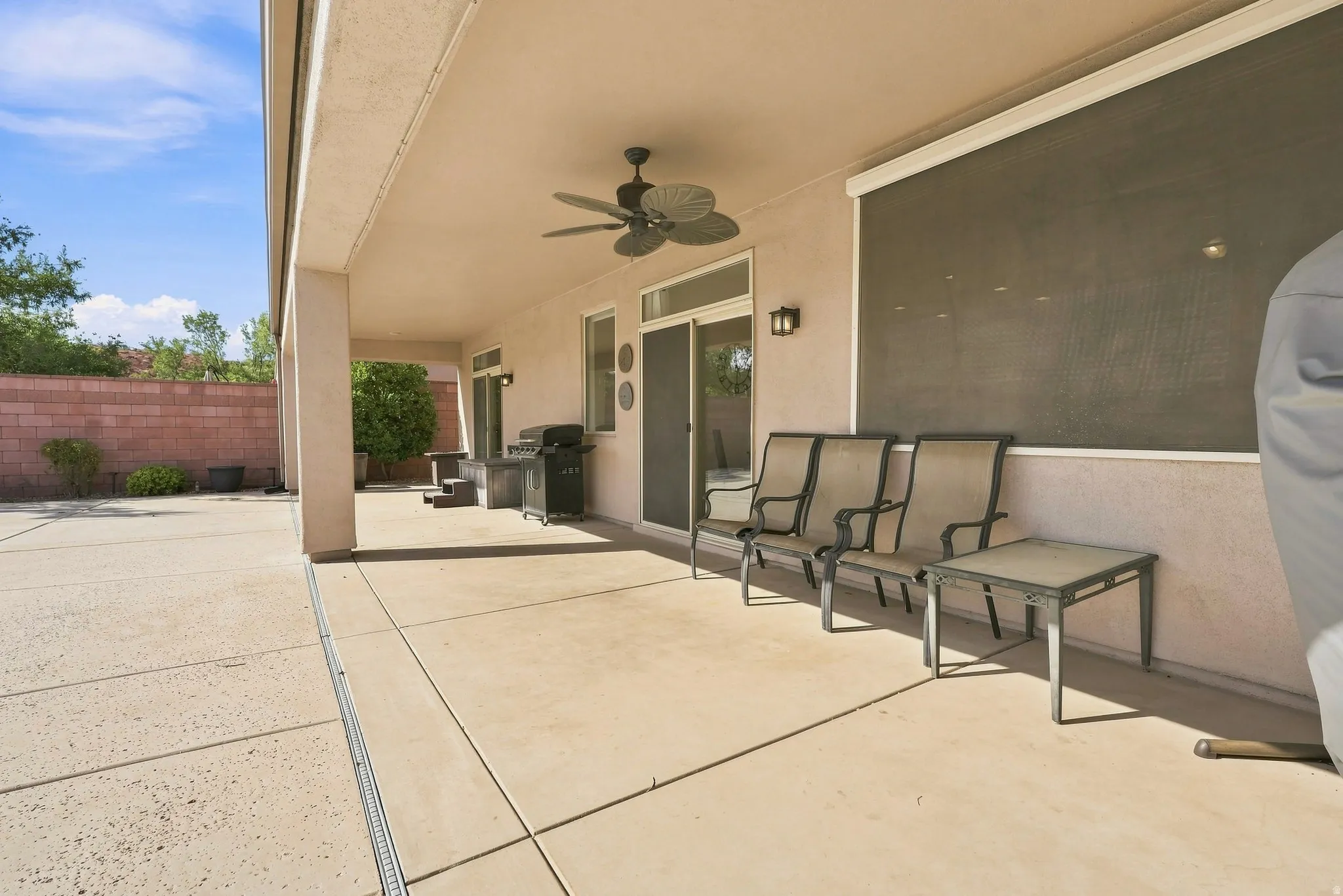 Covered patio featuring a ceiling fan, dual sliding glass doors, exterior wall sconces, and a block wall perimeter