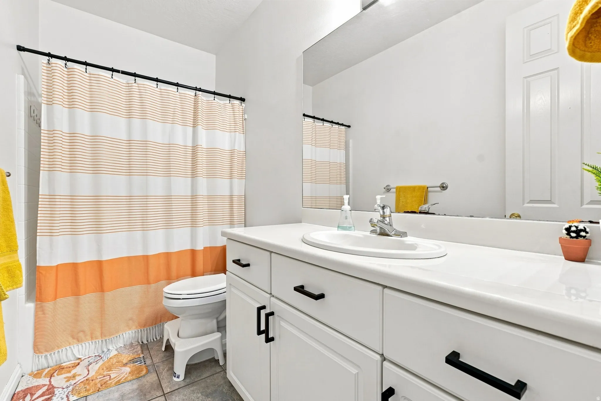 Bright bathroom featuring a single vanity with an integrated sink, white countertop, white cabinetry with black hardware, and an expansive mirror
