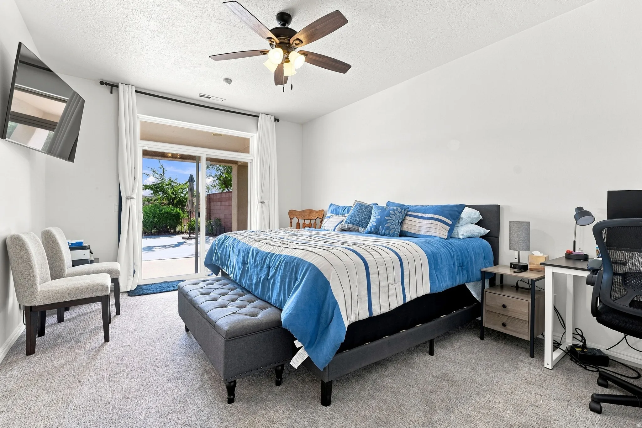 White-painted interior space with light-toned carpeting, featuring a ceiling fan with integrated lighting and a sliding glass door providing access to the outdoor area
