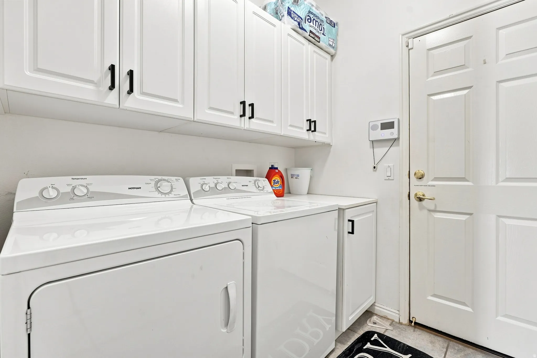 Laundry room featuring white cabinetry with black hardware, white countertop, and tiled flooring