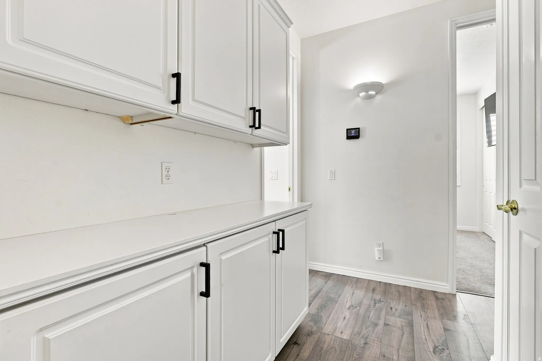White shaker-style cabinetry with matte black hardware, solid surface countertops, and wood-finish flooring