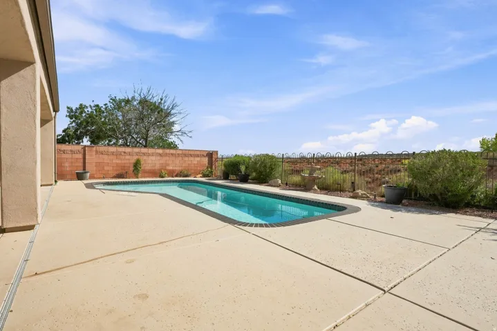 Backyard featuring a rectangular swimming pool with brick coping, expansive concrete patio, and a brick privacy wall