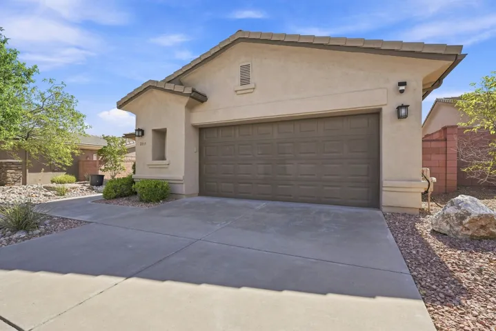 Stucco exterior with an attached garage featuring a panel door, concrete driveway, and desert-style landscaping