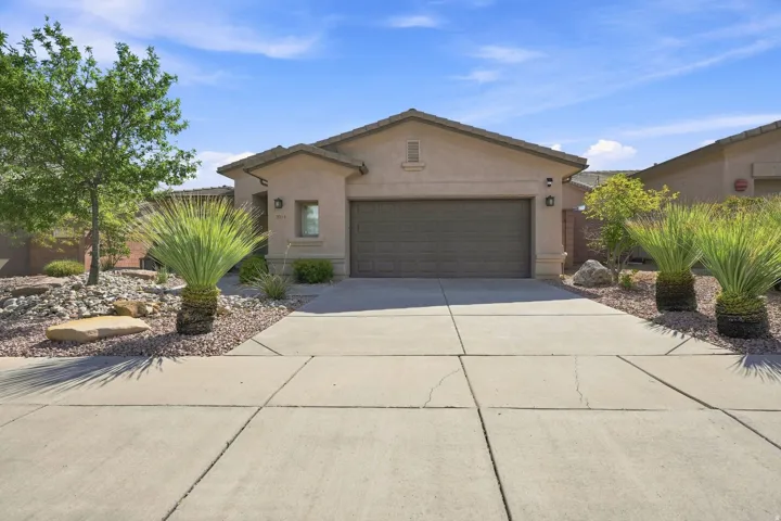 Stucco exterior featuring a two-car garage, concrete driveway, and xeriscape landscaping
