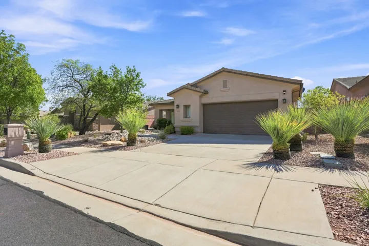 Desert landscape featuring mature trees and shrubbery, a concrete driveway, and a two-car garage