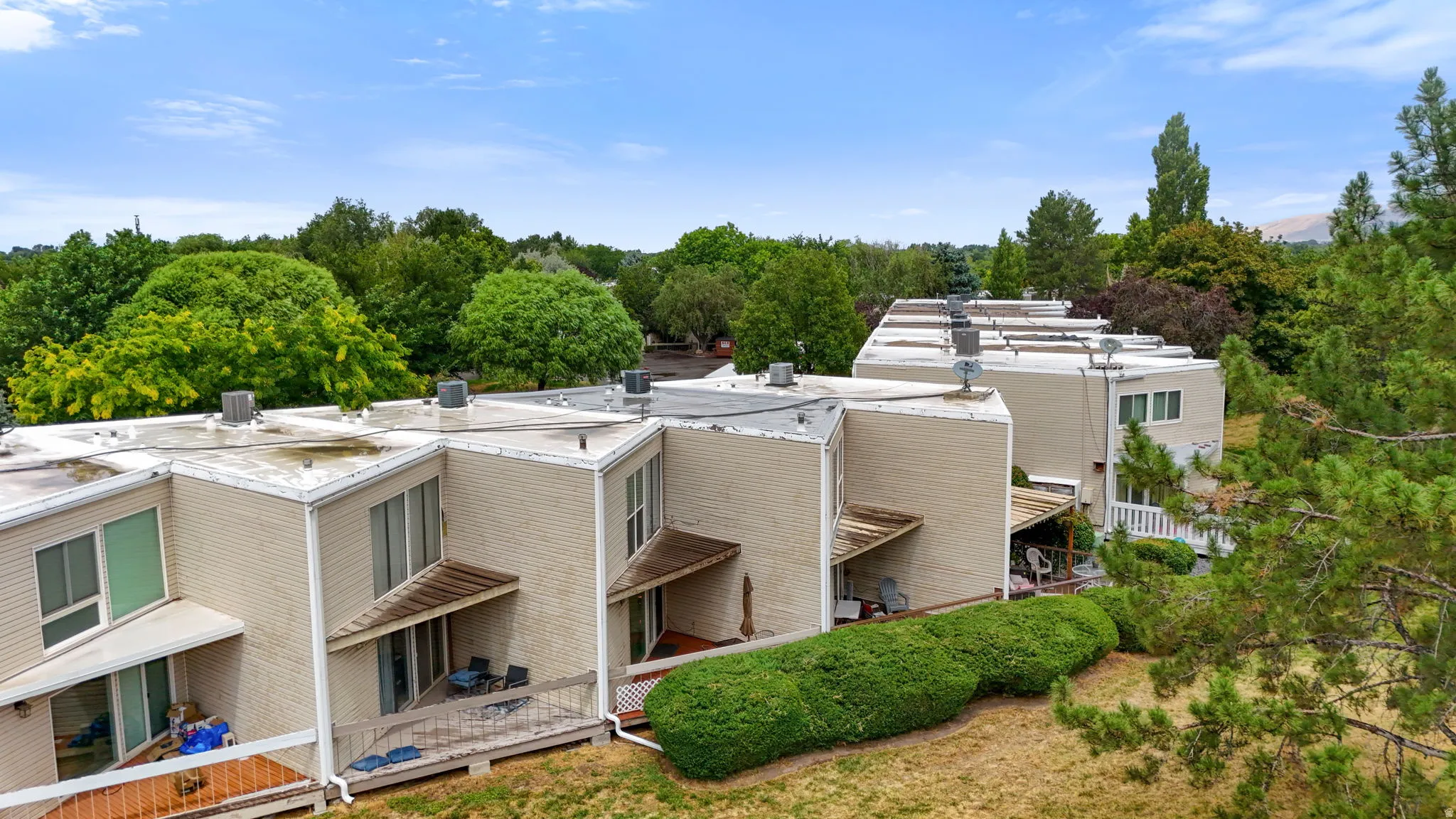 Townhome exteriors featuring light-colored siding, multiple private decks, and mature perimeter landscaping