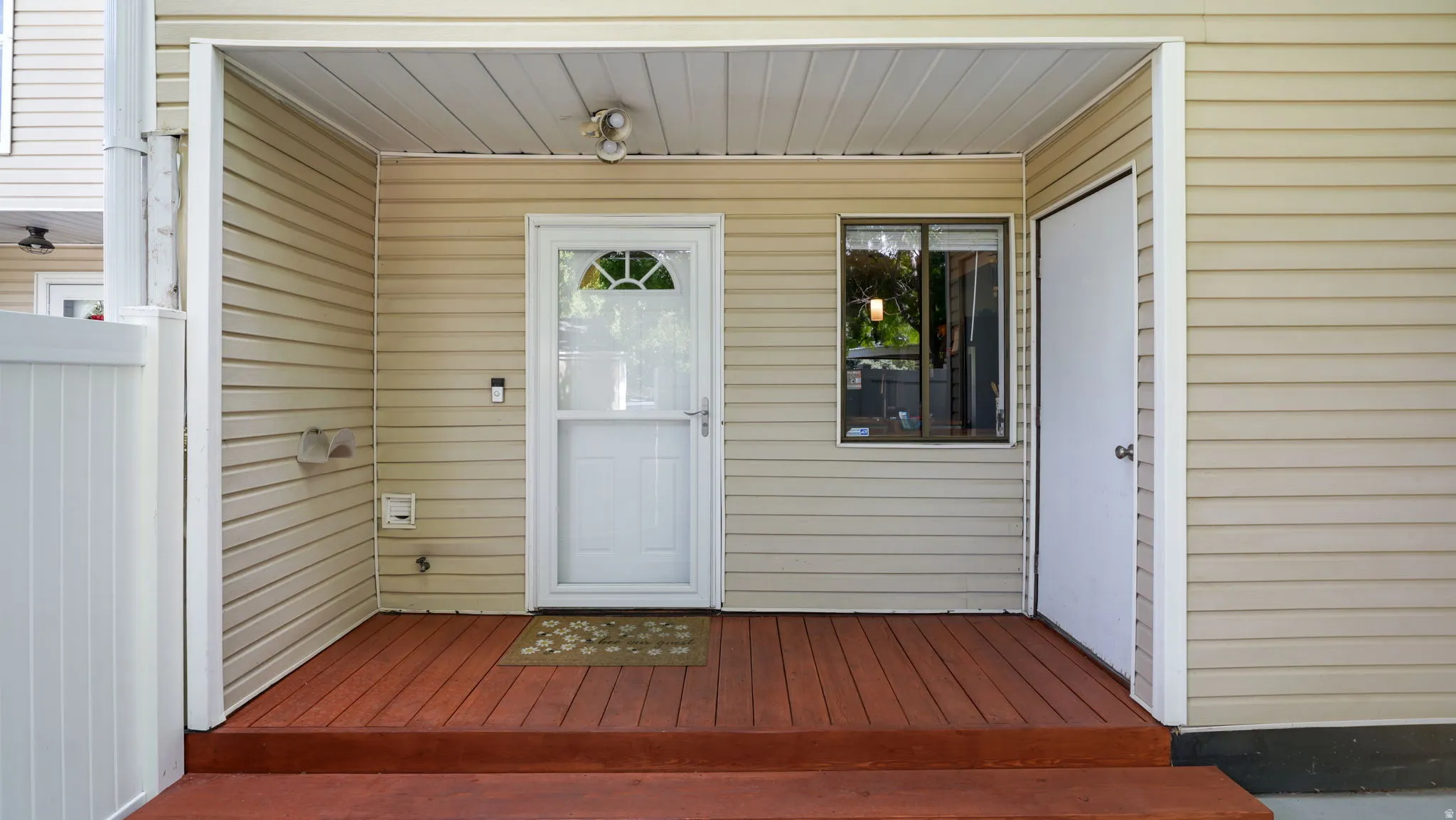 Covered entryway featuring beige vinyl siding and wood-finish decking